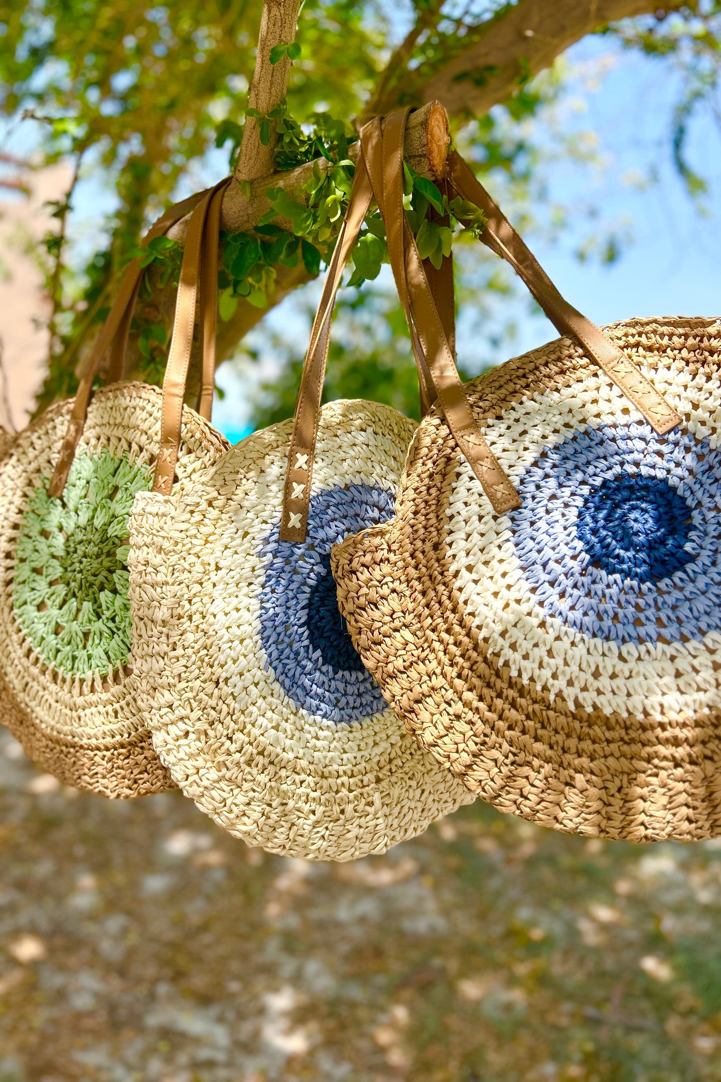 Three woven bags with blue and green designs hanging from a tree.