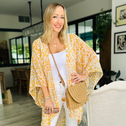 Cross body tan woven clutch bag with detachable cross body strap with pom pom. Worn with medium style kimono in yellow and grey